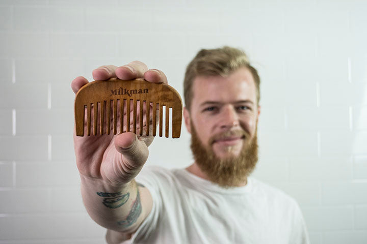 bearded man holding a wooden beard comb from Milkman Grooming Co