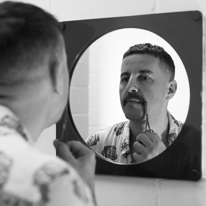 man trimming moustache in front of mirror