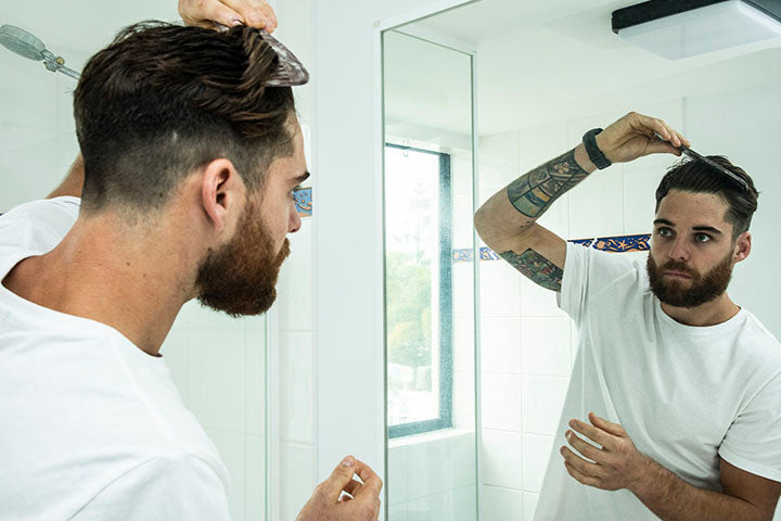 bearded man styling hair in the bathroom mirror