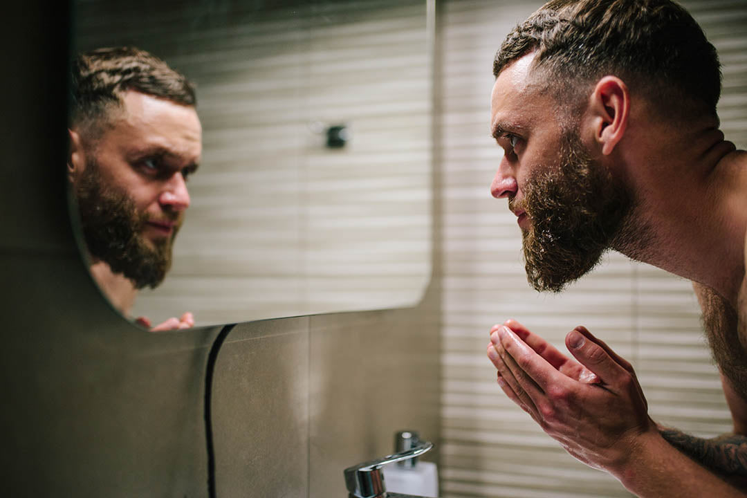 man washing beard in the mirror