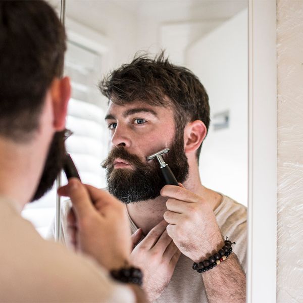 man holdings the double edge straight razor used by a bearded man looking in the mirror